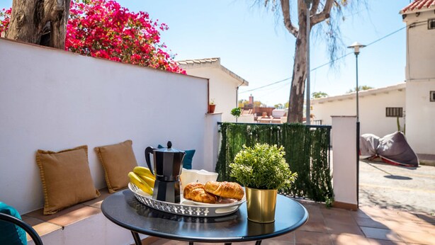 Een terras met een ontbijttafel, compleet met croissants en bananen, een koffiepot en een bloempot.