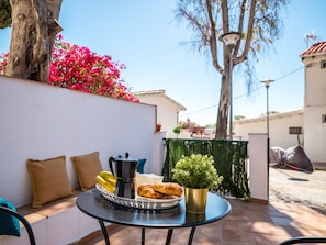 Eine Terrasse mit Tisch, gedeckt für das Frühstück, mit Croissants, Bananen, einer Kaffeekanne und einem Blumentopf.