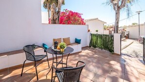 Een terras met twee wicker stoelen, een kleine ronde tafel met een plant en een bank met kussens.