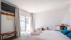Een slaapkamer met een groot bed, een bureau, een stoel, een klein tafeltje en een raam met gordijnen.