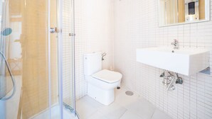 Een moderne badkamer met een douchecabine van glas, een wit toilet en een wastafel met een spiegel erboven.