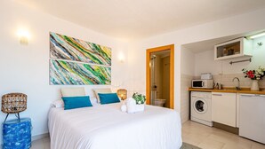 Een slaapkamer met een bed, een wasmachine en een kitchenette.