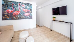 Ett modernt vardagsrum med en stor tavla som föreställer flamingos, en platt-TV och ett minimalistiskt konsolbord.