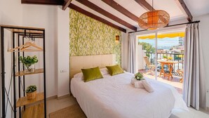 Un dormitorio con una cama grande, un perchero de madera con plantas, un papel tapiz estampado y un balcón con mesa y sillas.
