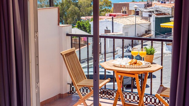 Un balcón con mesa de madera, dos sillas y vista panorámica de la ciudad.