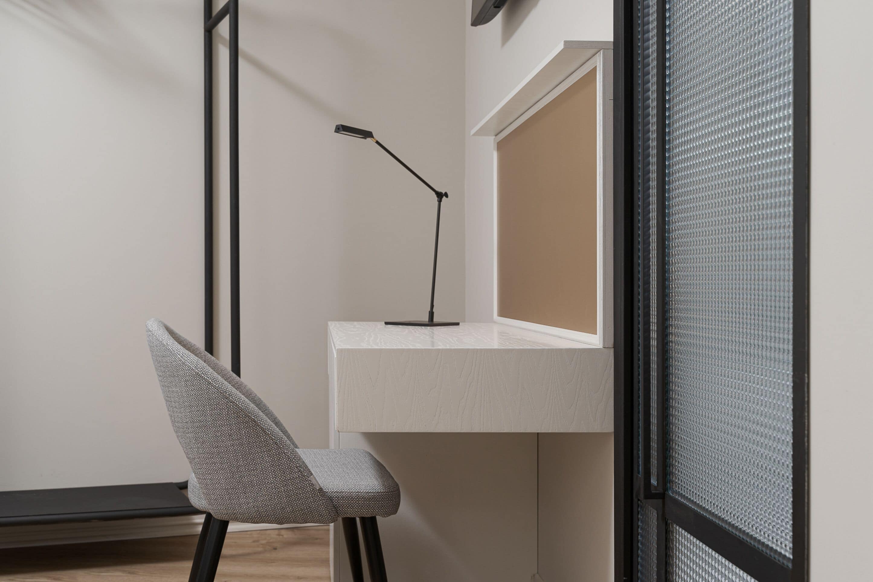A corner of a room with a white desk, a chair, and a black floor lamp.
