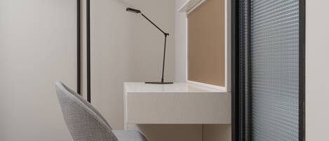A corner of a room with a white desk, a chair, and a black floor lamp.