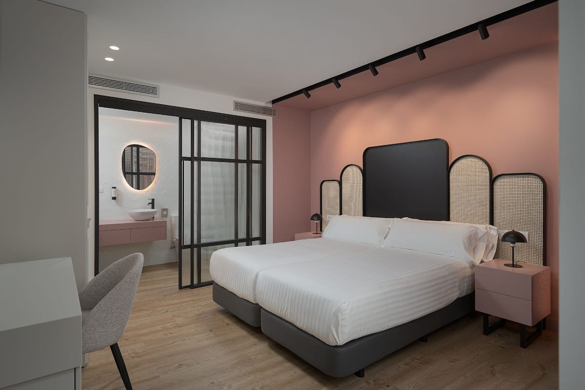 A modern bedroom with a large bed, a bedside table, a chair, and a bathroom visible through a sliding door.