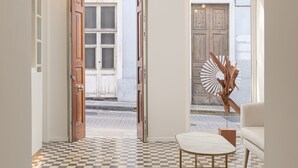 A hallway with a checkered floor, wooden doors, and a white armchair. - Boutique Hotel Cordial La Niña de Vegueta (Las Palmas de Gran Canaria)