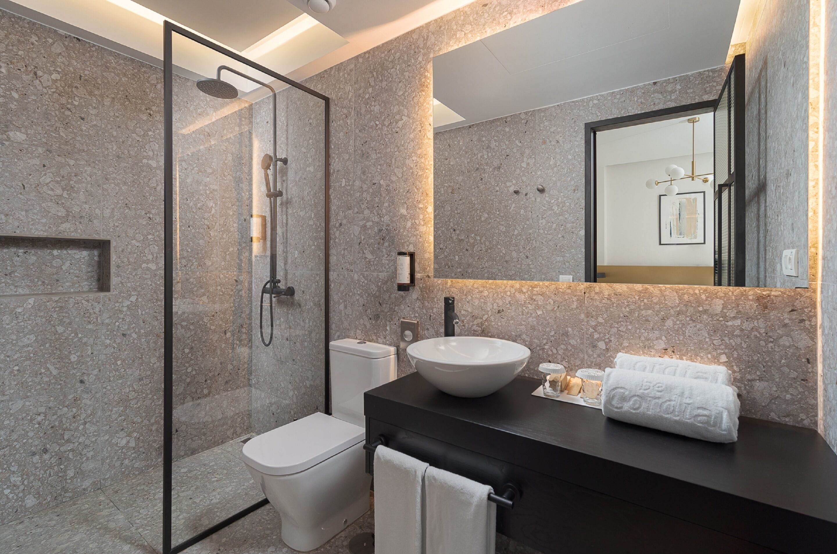 A modern bathroom with a glass-enclosed shower, a white toilet, a black vanity with a large sink, and a towel rack.