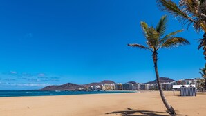 A beach with a palm tree, clear blue sky, and buildings in the background. - Boutique Hotel Cordial La Niña de Vegueta (Las Palmas de Gran Canaria)
