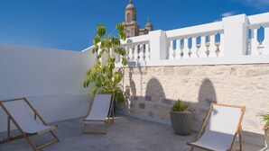 A rooftop terrace with white walls, a stone wall, and a view of a church. There are two lounge chairs and a potted plant. - Boutique Hotel Cordial La Niña de Vegueta (Las Palmas de Gran Canaria)