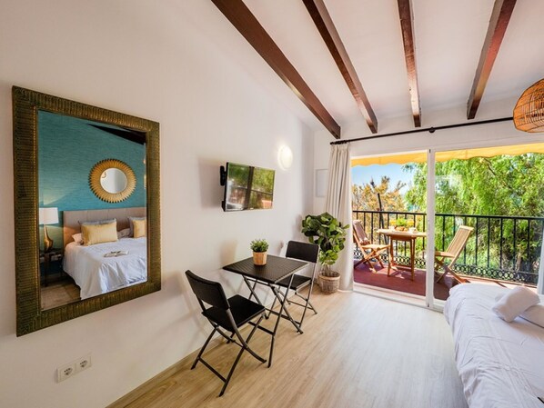 Un dormitorio con cama, escritorio y silla. Tiene un balcón con mesa y sillas.