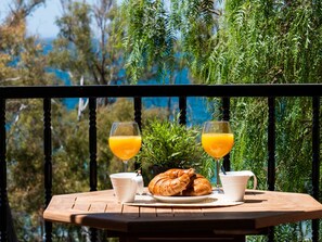 Una mesa con cruasanes, dos vasos de jugo de naranja y tazas blancas al aire libre.