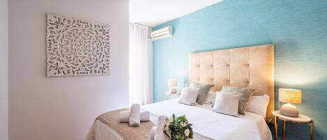 Un dormitorio con una cama grande, un adorno en la pared, una pared de acento azul y piso de madera.