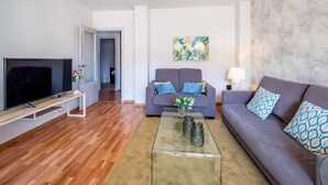 A modern living room with a flat-screen TV, two sofas, a glass coffee table, and a painting on the wall. - Sunset Malaga Apartments - Maestranza 8d2 (Málaga)