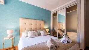 A hotel room with a large bed, a bedside table with a lamp, a wardrobe with a mirror, and a blue wall. - Sunset Malaga Apartments - Maestranza 8d2 (Málaga)