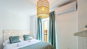 A bedroom with a wooden headboard, a bed with green bedding, a wicker hanging light fixture, and a view through a window with curtains.