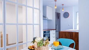 A modern kitchen with a stainless steel refrigerator, a dining table with a basket of flowers and a glass of orange juice, and a blue chair.