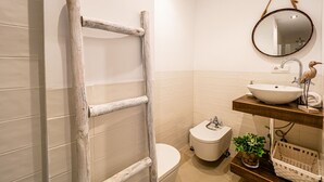 A bathroom with a wooden ladder, a toilet, a sink with a mirror, and a basket.