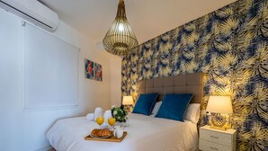A bedroom with a bed, bedside tables, a nightstand, a decorative lamp, and a wall with a leaf pattern.