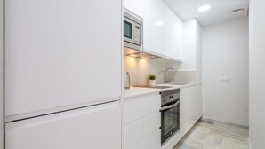 A compact kitchen with white cabinetry, a built-in microwave, a stainless steel oven, and a small countertop with a plant. - Sunset Malaga Apartments - Blaser 2E (Málaga)