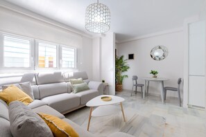 Un salon moderne avec un canapé gris, une petite table blanche et un coin repas comprenant deux chaises.