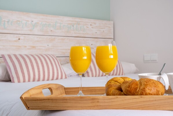 A wooden tray with croissants and two glasses of orange juice on a bed.