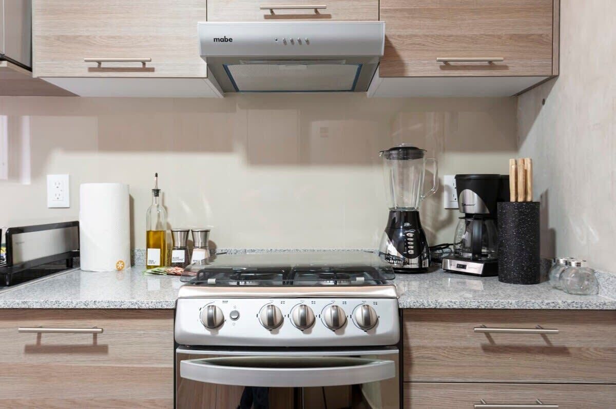A kitchen with a gas stove, a coffee maker, and a blender on the countertop.