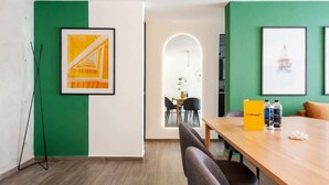 Een moderne kantoorruimte met groene wanden, een houten tafel, kunstwerken in lijsten en een staande lamp.