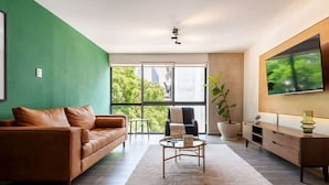Een moderne woonkamer met een bruine leren bank, een ronde salontafel en een grote flatscreen televisie die aan de muur is bevestigd.