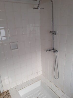 Une salle de bain avec des carreaux blancs, une douche et des toilettes.
