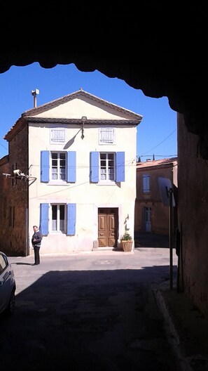 Un bâtiment à deux étages avec des volets bleus, une porte centrale et un petit jardin.
