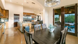Una cocina amplia con electrodomésticos modernos, un comedor con una gran mesa de madera y vistas al exterior a través de amplios ventanales correderas.