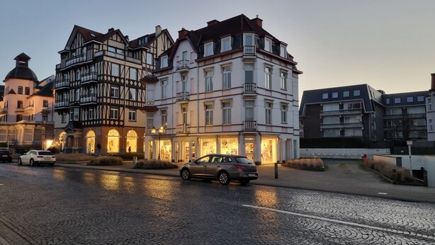 Ein historisches Gebäude im traditionellen europäischen Stil, mit mehreren Stockwerken, einem markanten Balkon und einem Geschäft im Erdgeschoss.