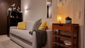Ein modernes Wohnzimmer mit einem grauen Sofa, gelb-grauen Kissen, einem kleinen Holztisch mit einer Pflanze und dekorativen Wandleuchten.