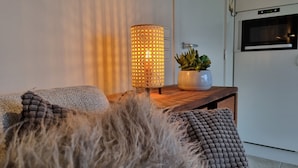 Ein gemütlicher Wohnbereich mit einer strukturierten Couch, einer dekorativen Lampe und einem Blumentopf auf einem Holztisch.