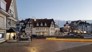 A traditional European town square with historic buildings, a central open space, and a shop named "Zee-Linde". - Studio De Haan - Netflix, Gelmatras en Zwembad (De Haan)