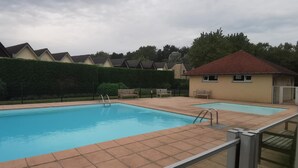 Ein rechteckiger Pool mit Fliesen umgeben, umgeben von einer Hecke und einer Reihe von Häusern.