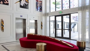 A modern lobby with a red sectional sofa, marble flooring, elevators, and large windows with a view of the outside. - UMA House by Yurbban South Beach (Miami Beach)