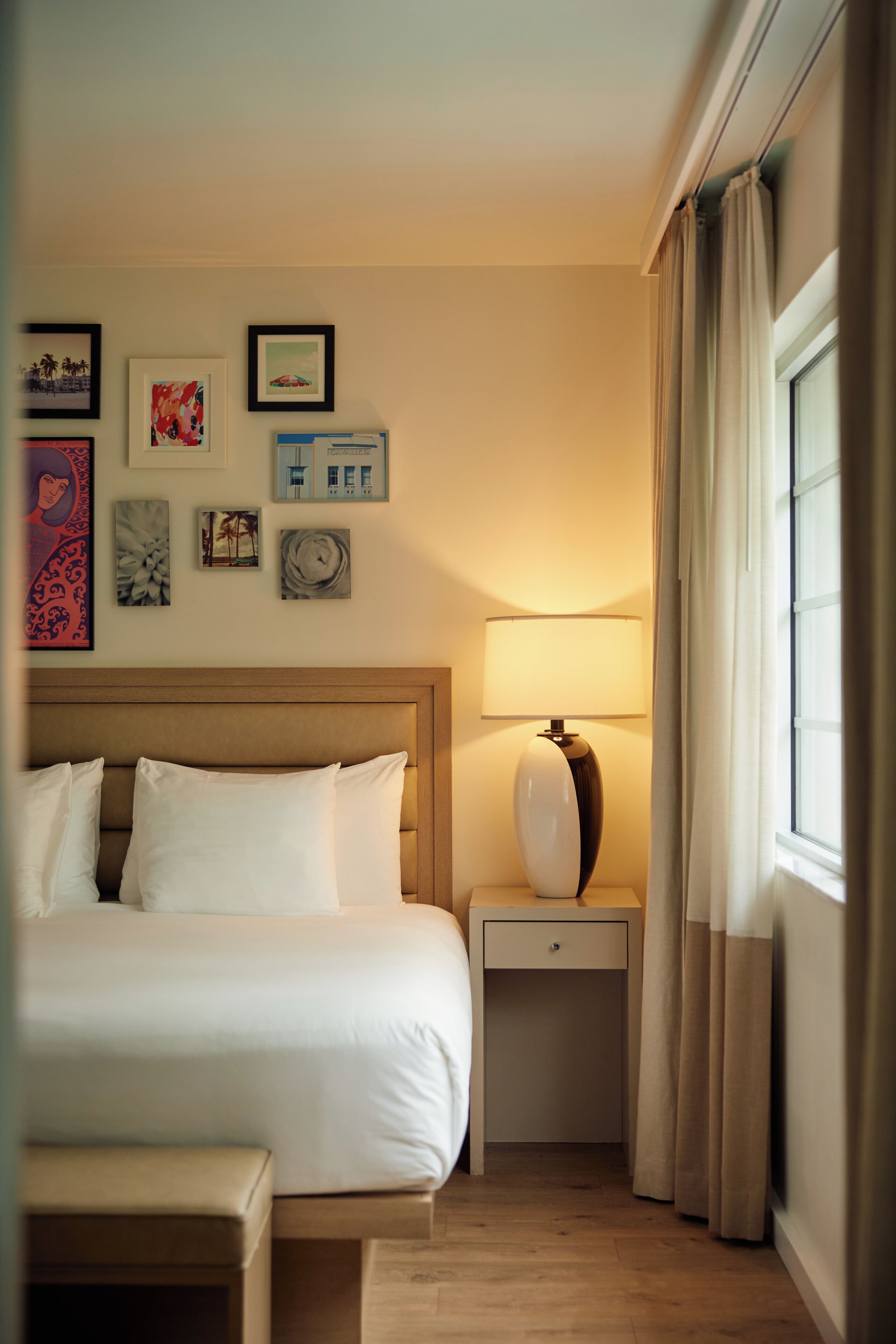 A hotel room with a bed, bedside tables, a lamp, and artwork on the wall.