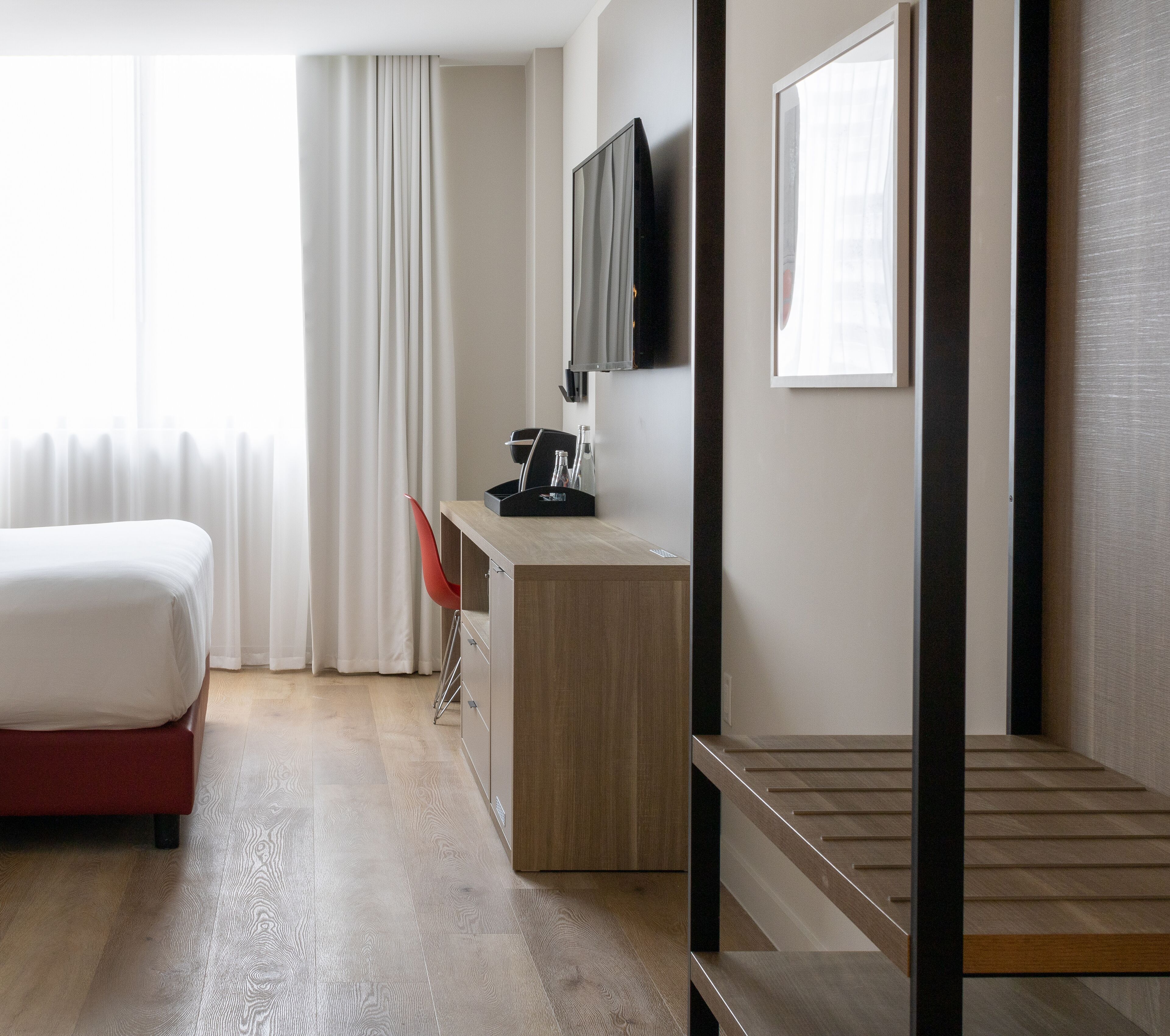 Ett hotellrum med en säng, ett skrivbord, en stol, en tv och en trappa.