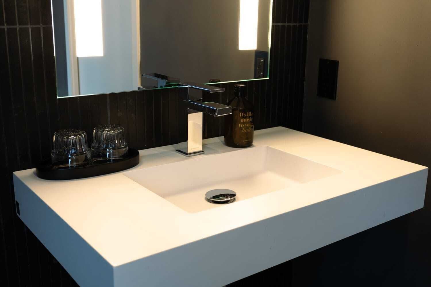 A modern bathroom with a white sink, a mirror, and a glass soap dispenser.