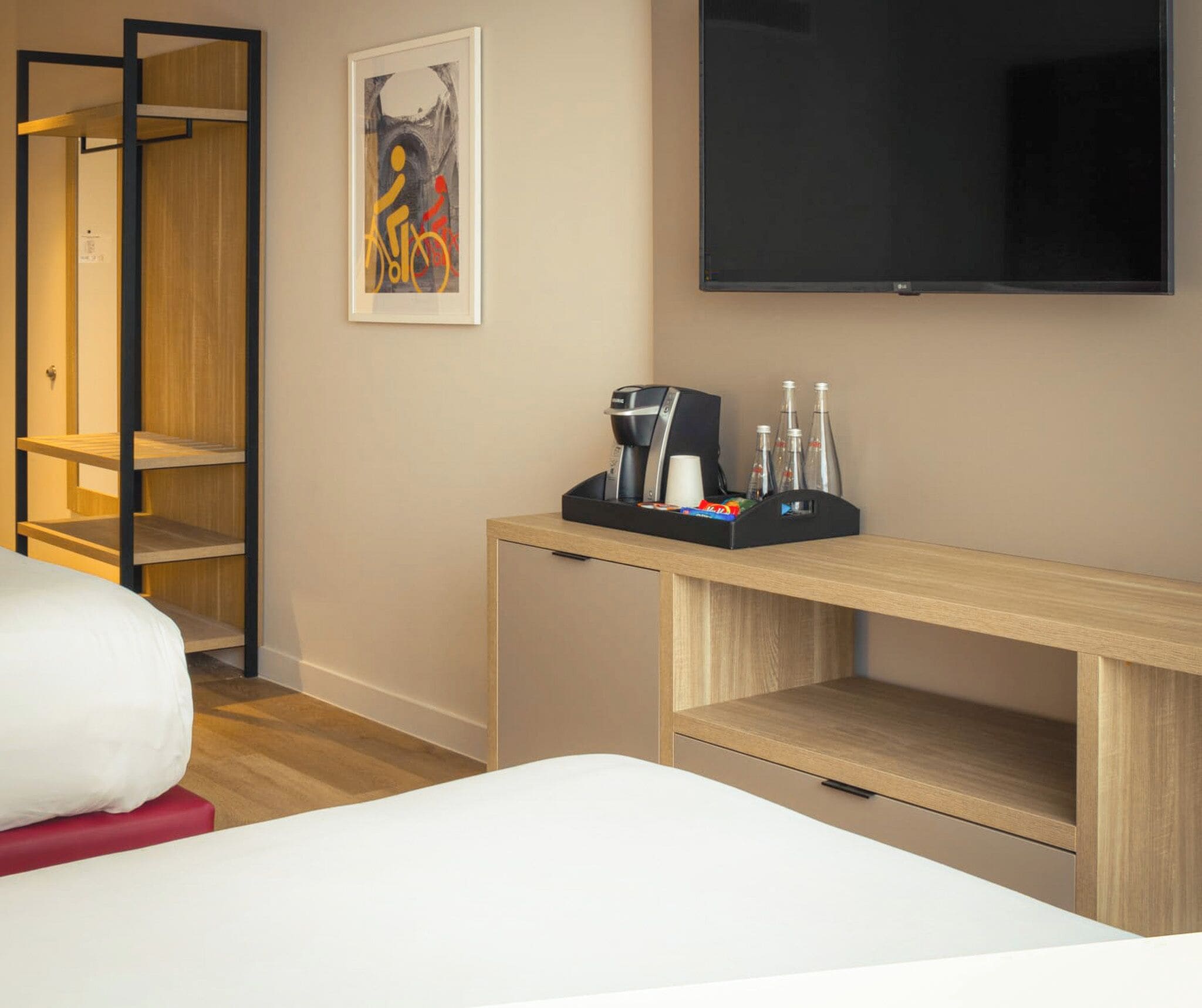 A hotel room with a bed, a desk with a coffee maker, a TV, and a wardrobe.