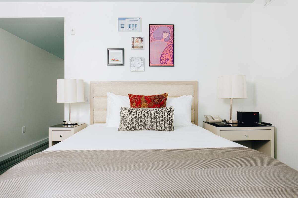 A hotel room with a large bed, two bedside tables, a nightstand, a lamp, a phone, and a wall with framed pictures.