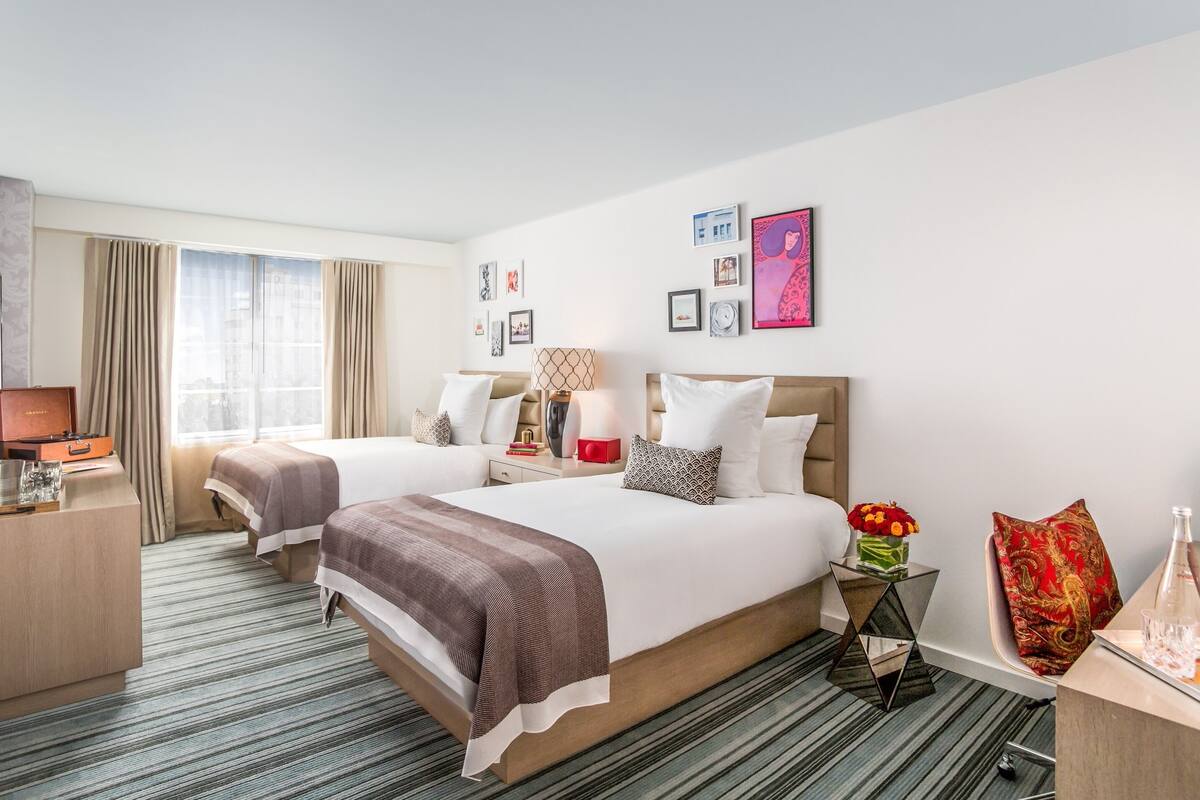 A hotel room with two beds, a desk, a chair, a TV, and a window with curtains.
