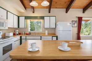 A kitchen with wooden cabinets, a white refrigerator, a sink, and a window with a view of greenery. - Summer Pool | Hot Tub | Fenced | Dogs | Firepit (Leavenworth)