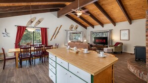 A spacious living area with a wooden ceiling, a dining table with chairs, a sofa, a TV, and a fireplace.