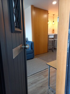 A room with a wooden door, a blue sofa, a small table, and a kitchen area with a countertop and hanging lights. - CASA MIRA DOURO marina beach 5mnts on foot caves, Porto bridge 5mnts by car (Vila Nova de Gaia)