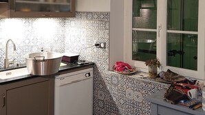Cocina compacta con lavavajillas, pileta y ventana con cortinas verdes.